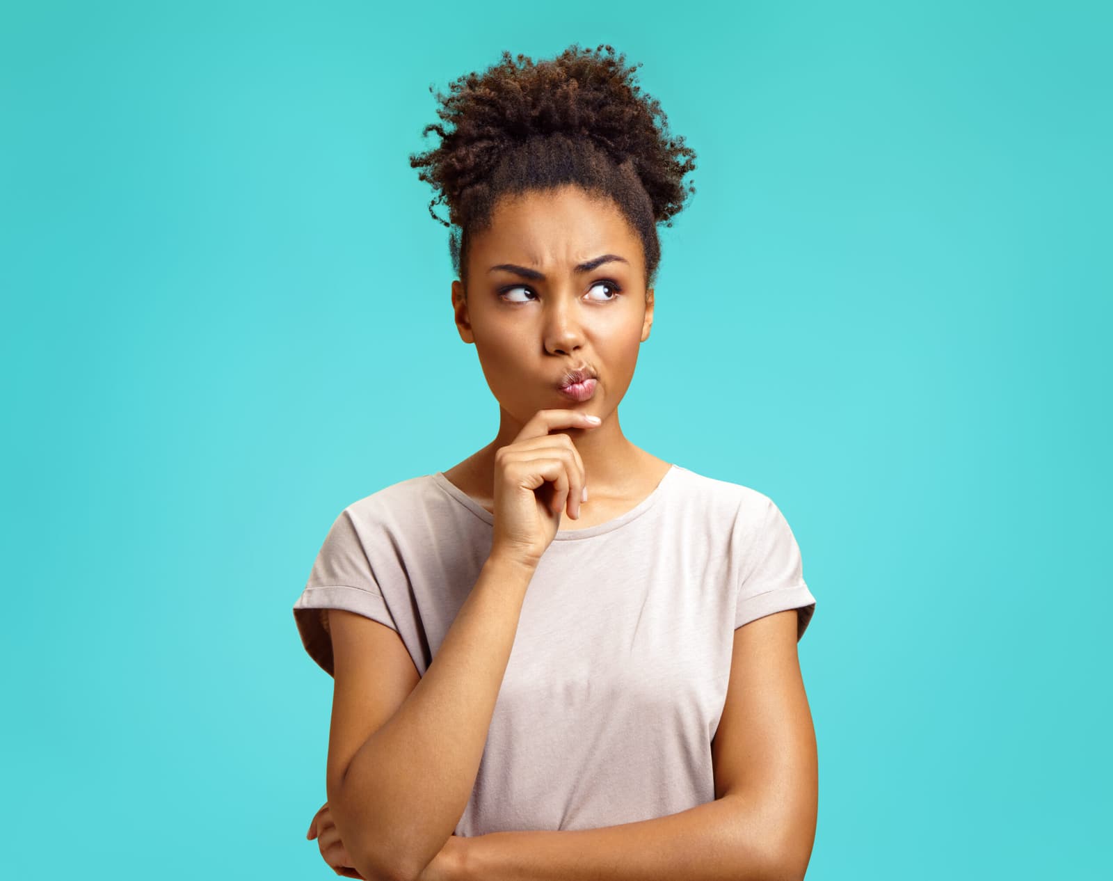 Thoughtful young woman with her finger on her chin against a turquoise background.