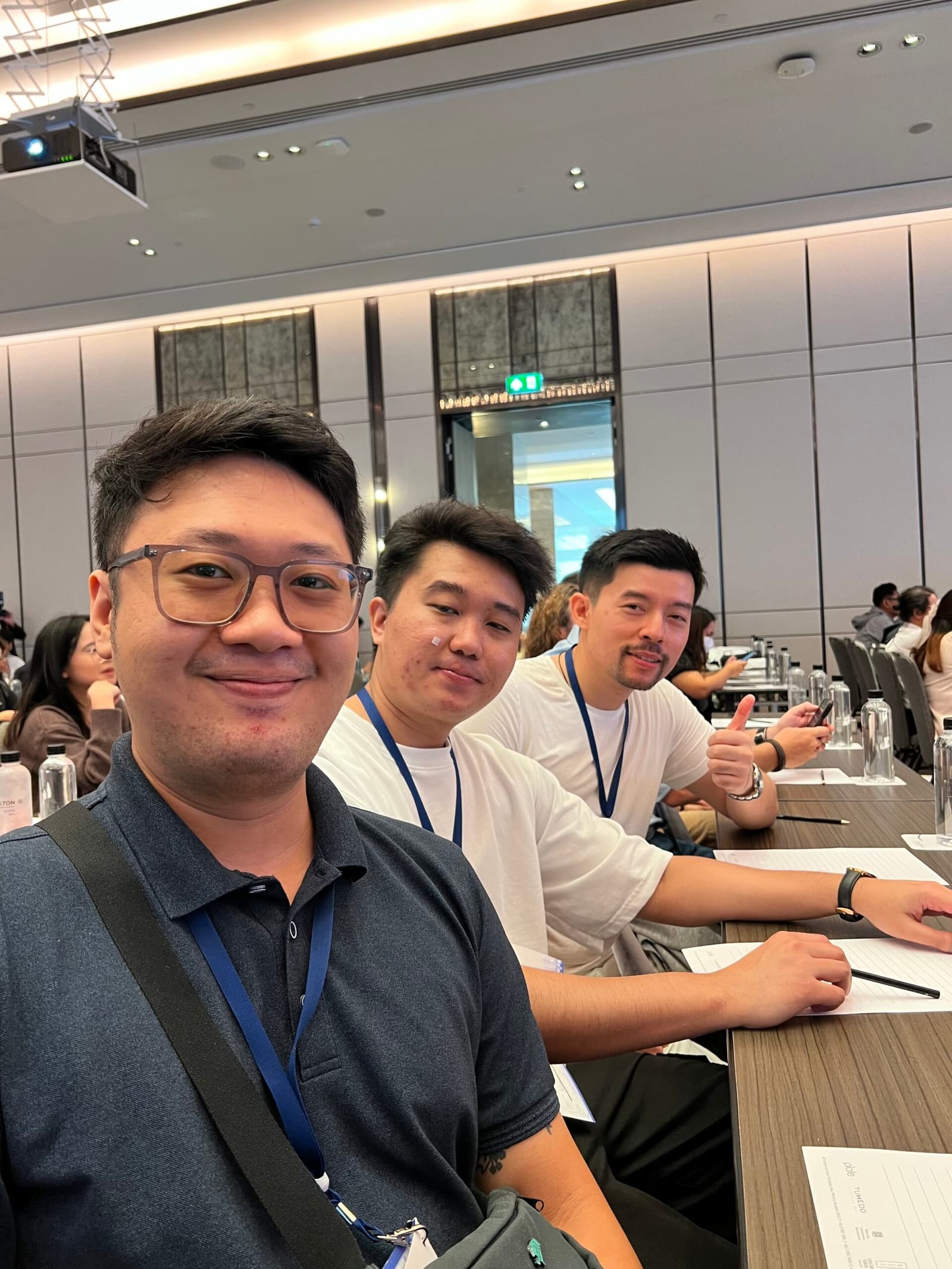 Three men smiling at a conference table, one giving a thumbs-up.