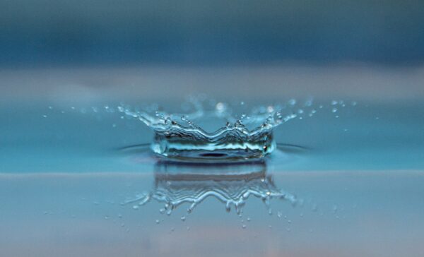Crown-shaped water splash and its reflection on a calm blue surface.