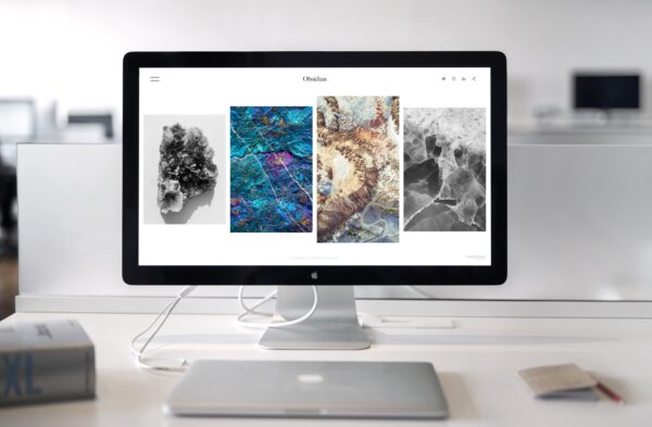 iMac monitor displaying an image-heavy website layout on a white office desk.
