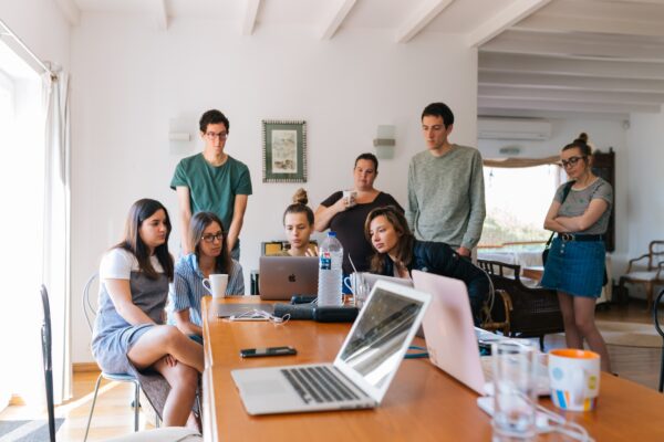 A group of people gathered around laptops on a wooden table.