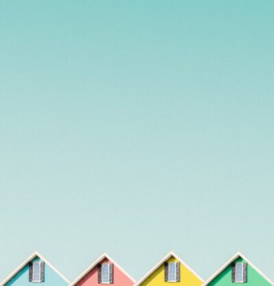 Four pastel-coloured house gables with windows against a pale turquoise sky.