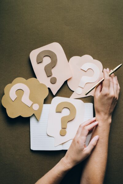 Hands holding a pen next to paper speech bubbles containing question marks.