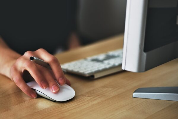 Hand holding a pen while using a white computer mouse on a desk.