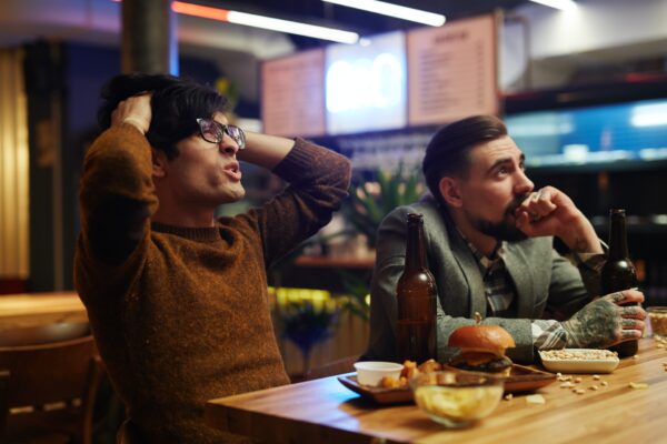 Two frustrated men looking stressed and disappointed while sitting at a bar.