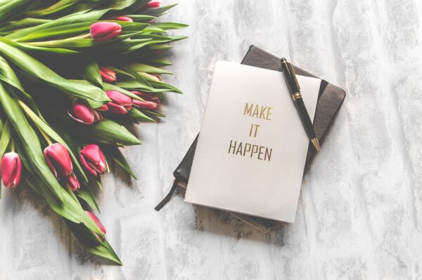 Pink tulips next to a 'MAKE IT HAPPEN' notebook and pen.